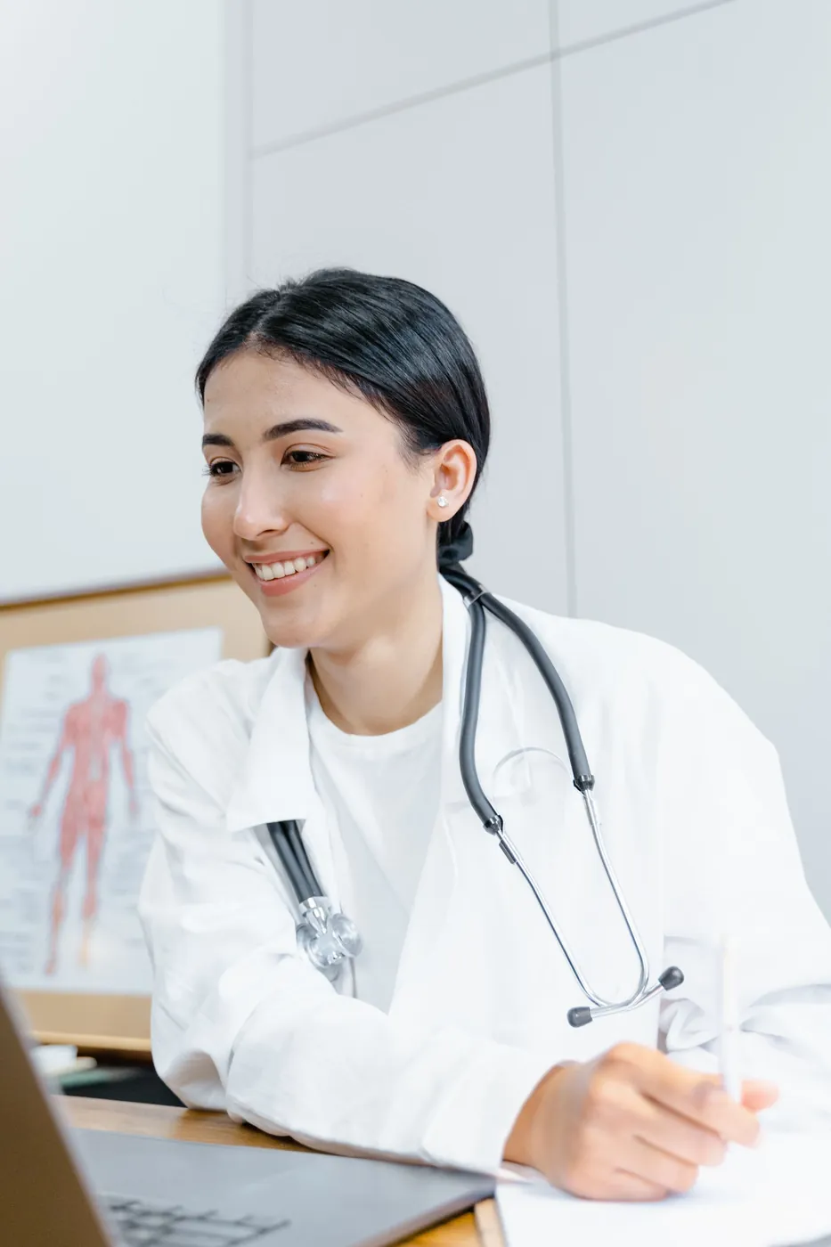 Doctora sonriendo mientras trabaja en su laptop dentro del consultorio